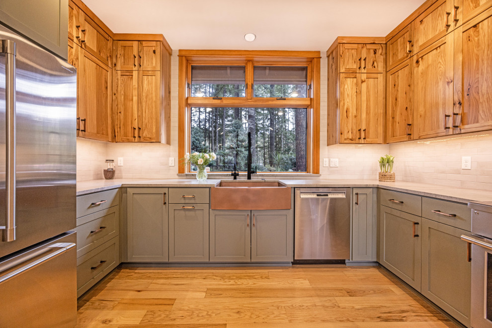 Example of a large mountain style u-shaped light wood floor and brown floor eat-in kitchen design with a farmhouse sink, shaker cabinets, quartzite countertops, gray backsplash, ceramic backsplash, stainless steel appliances, a peninsula and gray countertops