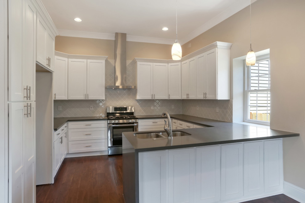 Photo of a mid-sized transitional u-shaped eat-in kitchen in New Orleans with an undermount sink, shaker cabinets, white cabinets, quartz benchtops, white splashback, glass sheet splashback, stainless steel appliances, medium hardwood floors, a peninsula, brown floor and grey benchtop.