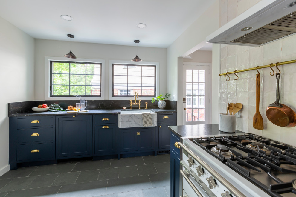 Photo of a small u-shaped separate kitchen in New York with a farmhouse sink, shaker cabinets, blue cabinets, granite benchtops, white splashback, white appliances, slate floors, no island, grey floor and black benchtop.