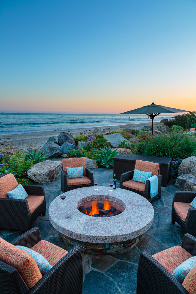 This is an example of a beach style backyard patio in Santa Barbara with a fire feature, natural stone pavers and no cover.