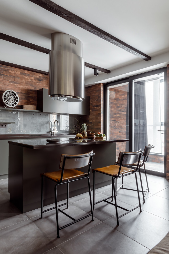 Design ideas for a mid-sized industrial galley open plan kitchen in Other with flat-panel cabinets, grey cabinets, solid surface benchtops, grey splashback, glass sheet splashback, porcelain floors, with island, grey floor and black benchtop.