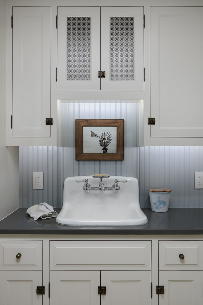 Country laundry room in Oklahoma City with a farmhouse sink, shaker cabinets, white cabinets, solid surface benchtops, blue walls, limestone floors, an integrated washer and dryer, white floor and grey benchtop.