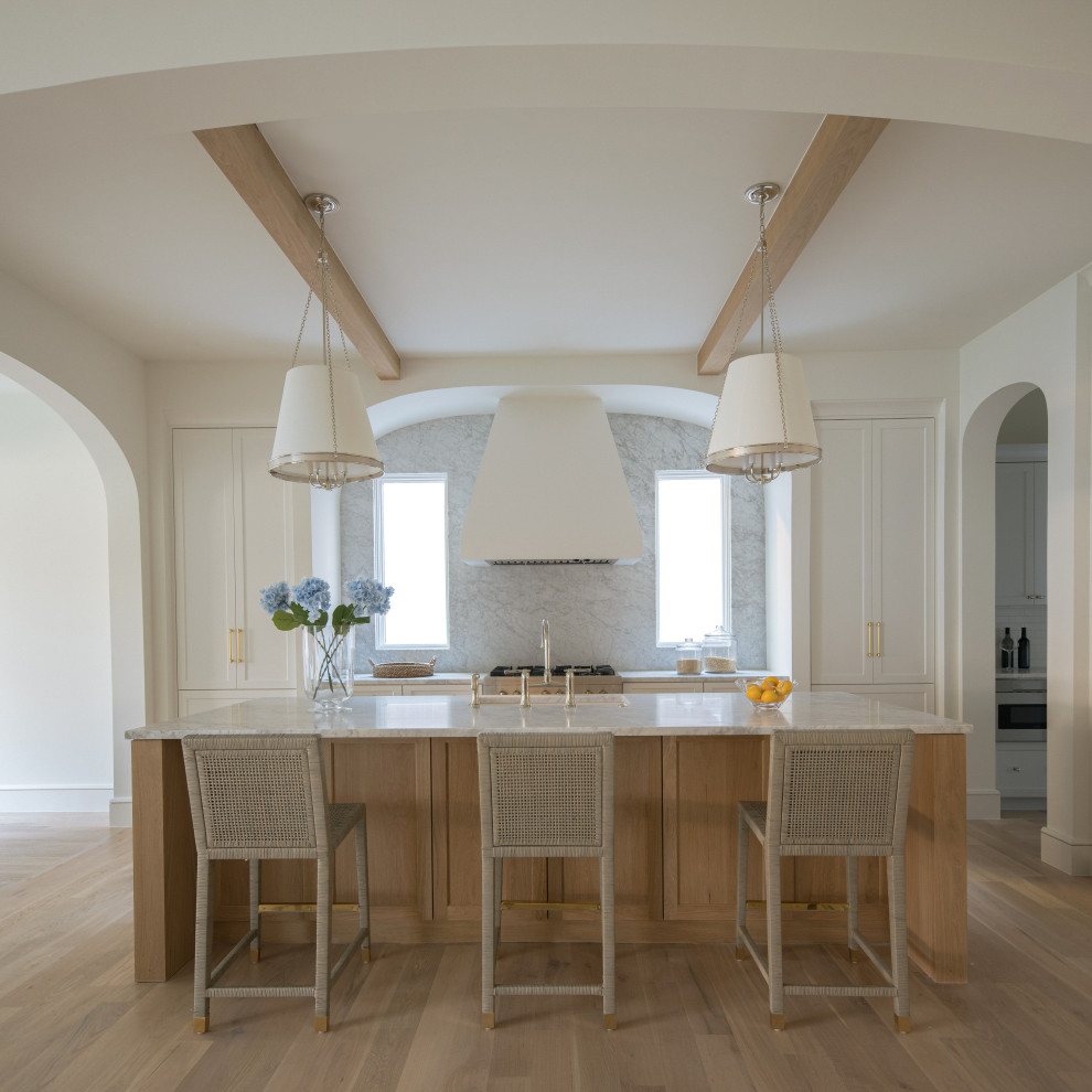 Photo of a beach style single-wall eat-in kitchen in Dallas with an undermount sink, shaker cabinets, white cabinets, marble benchtops, grey splashback, stone slab splashback, stainless steel appliances, light hardwood floors, with island, beige floor, grey benchtop and exposed beam.