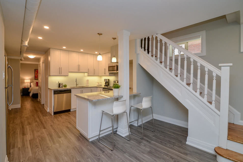 Open concept kitchen - mid-sized transitional u-shaped medium tone wood floor and gray floor open concept kitchen idea with an undermount sink, shaker cabinets, white cabinets, granite countertops, stainless steel appliances and a peninsula