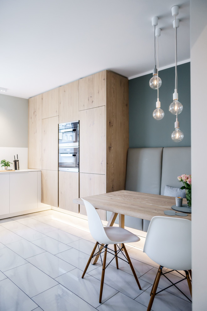 Photo of a mid-sized scandinavian l-shaped eat-in kitchen in Hamburg with flat-panel cabinets, white splashback, black appliances, marble floors, no island, white floor and white benchtop.