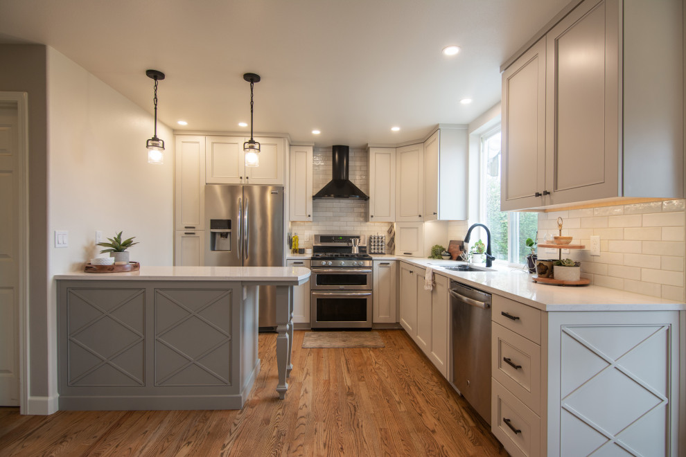 Mid-sized transitional l-shaped medium tone wood floor and brown floor kitchen photo with an undermount sink, recessed-panel cabinets, gray cabinets, quartz countertops, white backsplash, ceramic backsplash, stainless steel appliances, a peninsula and white countertops