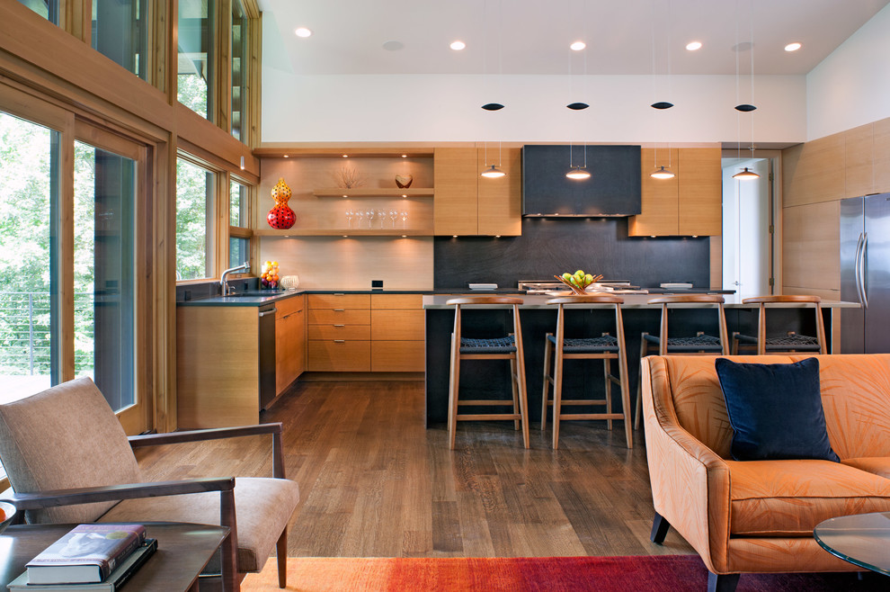 This is an example of a mid-sized contemporary l-shaped open plan kitchen in Charlotte with flat-panel cabinets, light wood cabinets, stainless steel appliances, dark hardwood floors, with island, solid surface benchtops, black splashback and brown floor.