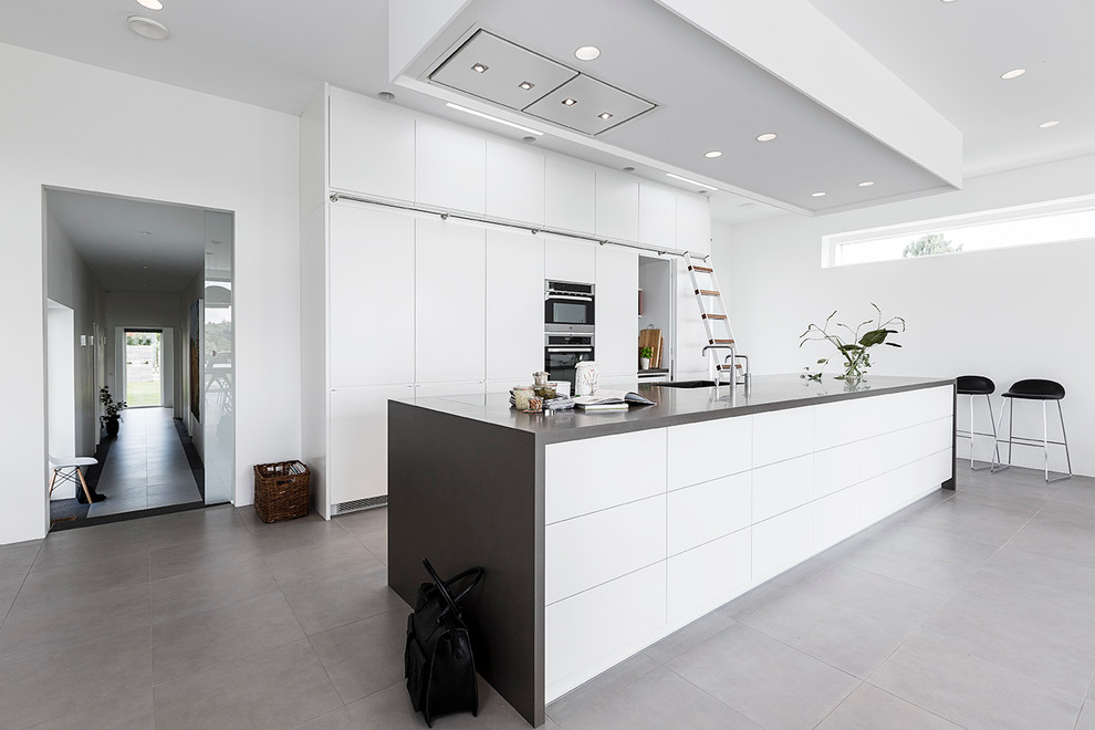 Large scandinavian galley eat-in kitchen in Aarhus with with island, flat-panel cabinets, white cabinets, an undermount sink, granite benchtops, stainless steel appliances and slate floors.