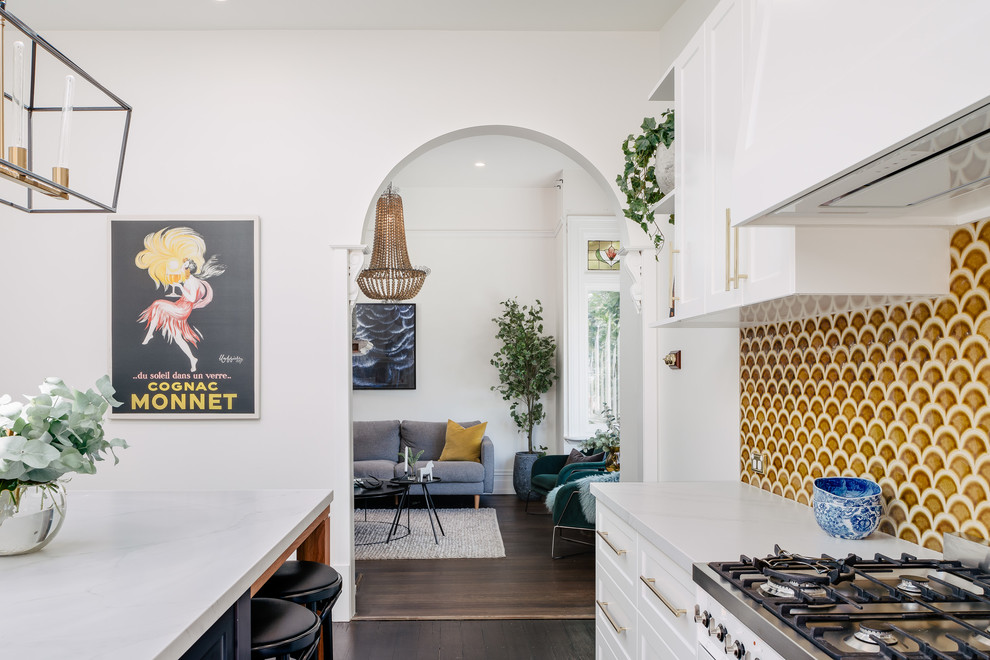 This is an example of a large transitional galley eat-in kitchen in Hobart with a farmhouse sink, shaker cabinets, white cabinets, quartz benchtops, yellow splashback, ceramic splashback, stainless steel appliances, dark hardwood floors, with island, brown floor and white benchtop.