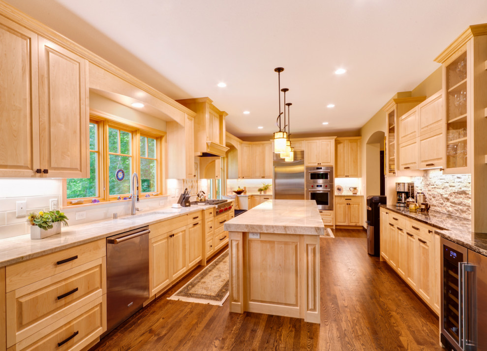 Photo of a large traditional l-shaped eat-in kitchen in Minneapolis with an undermount sink, raised-panel cabinets, light wood cabinets, quartzite benchtops, beige splashback, stone tile splashback, stainless steel appliances, medium hardwood floors, with island and beige benchtop.