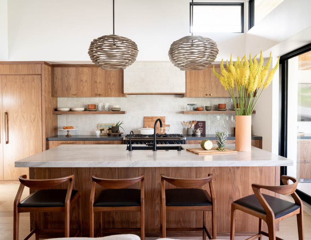 Zweizeilige Moderne Küche mit Unterbauwaschbecken, flächenbündigen Schrankfronten, hellbraunen Holzschränken, Küchenrückwand in Weiß, schwarzen Elektrogeräten, braunem Holzboden, Kücheninsel, braunem Boden und grauer Arbeitsplatte in Orange County