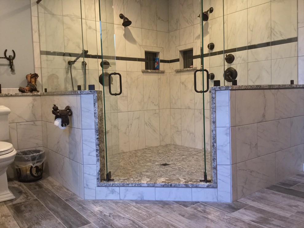 Corner shower - large rustic master gray tile and pebble tile porcelain tile corner shower idea with a two-piece toilet, gray walls, an undermount sink, granite countertops, beaded inset cabinets and dark wood cabinets