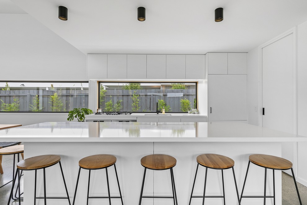 Design ideas for a large modern galley kitchen in Geelong with a double-bowl sink, flat-panel cabinets, white cabinets, quartz benchtops, window splashback, stainless steel appliances, concrete floors, with island and white benchtop.