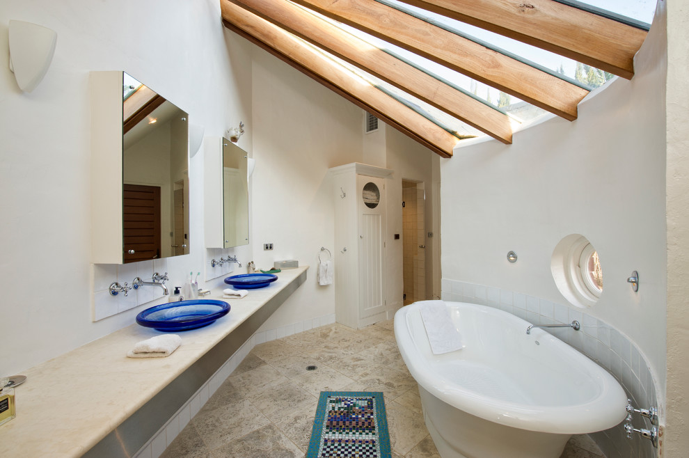 Photo of an eclectic bathroom in Adelaide with a vessel sink, a freestanding tub, beige tile, stone tile, white walls and travertine floors.