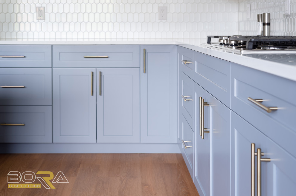 Example of a large transitional l-shaped medium tone wood floor and brown floor eat-in kitchen design in Seattle with an undermount sink, shaker cabinets, blue cabinets, quartz countertops, white backsplash, ceramic backsplash, stainless steel appliances, an island and white countertops