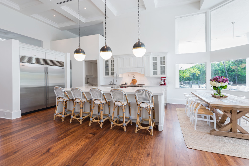Large country l-shaped open plan kitchen in Miami with shaker cabinets, white cabinets, quartz benchtops, white splashback, subway tile splashback, stainless steel appliances, medium hardwood floors, with island and brown floor.