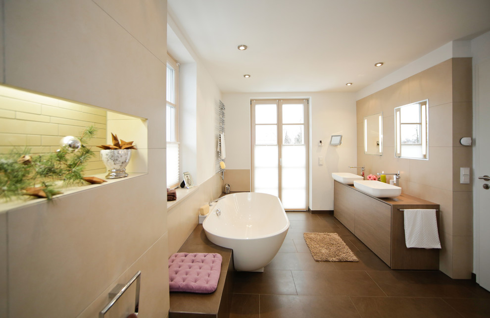 Duschbad mit flächenbündigen Schrankfronten, beigen Fliesen, braunen Fliesen, weißer Wandfarbe, Aufsatzwaschbecken, Waschtisch aus Holz, freistehender Badewanne, braunen Schränken, bodengleicher Dusche, Wandtoilette, braunem Boden und Falttür-Duschabtrennung in Munich