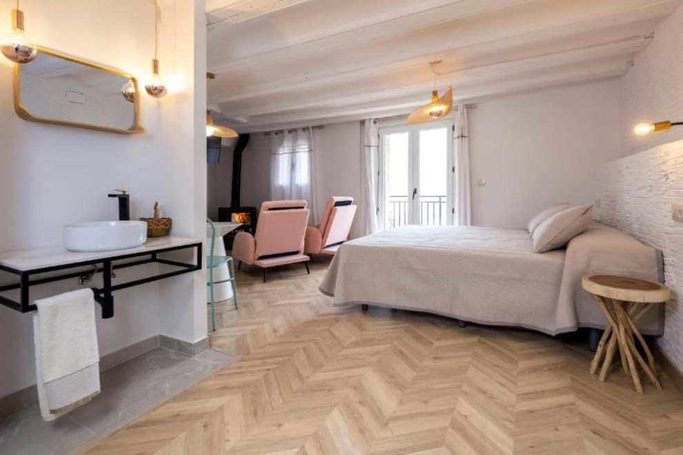 Immagine di una camera da letto stile loft scandinava con pareti bianche, parquet chiaro, camino ad angolo, travi a vista e pareti in mattoni
