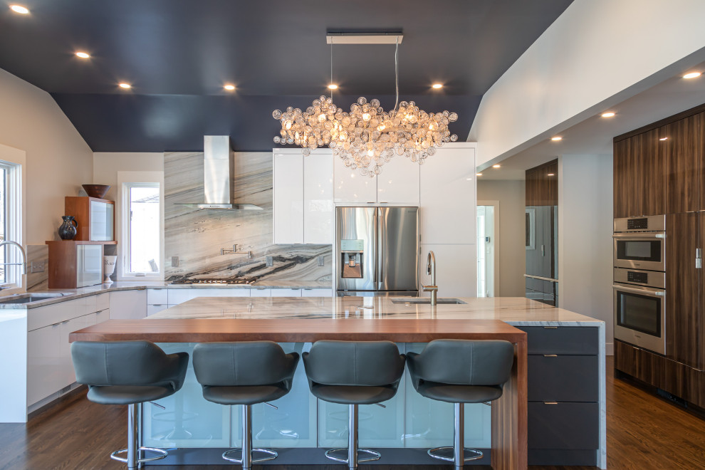 Photo of a mid-sized contemporary u-shaped open plan kitchen in Raleigh with an undermount sink, flat-panel cabinets, white cabinets, marble benchtops, grey splashback, marble splashback, stainless steel appliances, medium hardwood floors, with island, brown floor, grey benchtop and vaulted.