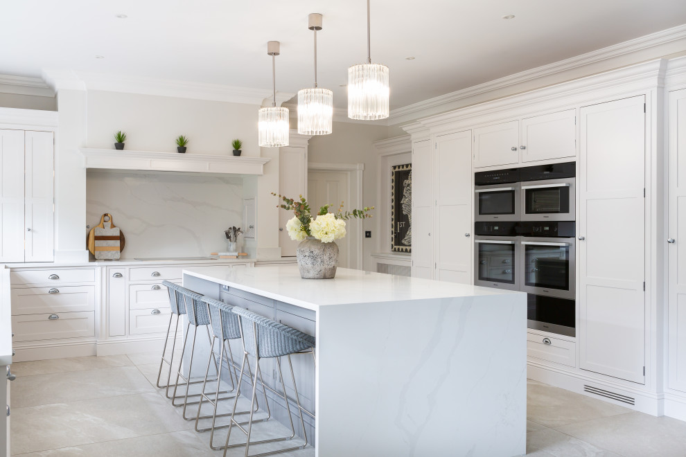 This is an example of a classic u-shaped kitchen in Essex with beaded cabinets, white cabinets, white splashback, stone slab splashback, stainless steel appliances, grey floors and white worktops.