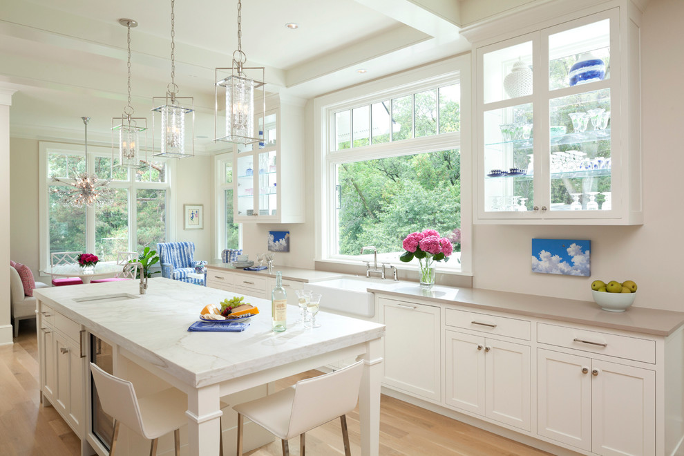 Inspiration for a mid-sized traditional open plan kitchen in Minneapolis with a farmhouse sink, shaker cabinets, white cabinets, light hardwood floors, with island, marble benchtops, white splashback, stone slab splashback and stainless steel appliances.