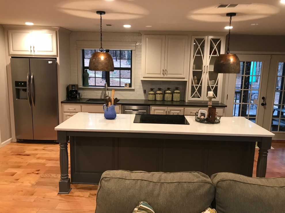 Example of a mid-sized transitional l-shaped medium tone wood floor and brown floor open concept kitchen design with an undermount sink, raised-panel cabinets, white cabinets, white backsplash, stainless steel appliances, an island and white countertops