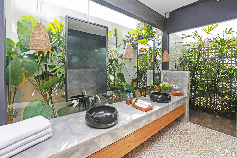 Inspiration for a tropical bathroom with flat-panel cabinets, medium wood cabinets, a curbless shower, a vessel sink, concrete benchtops, beige floor, an open shower and grey benchtops.