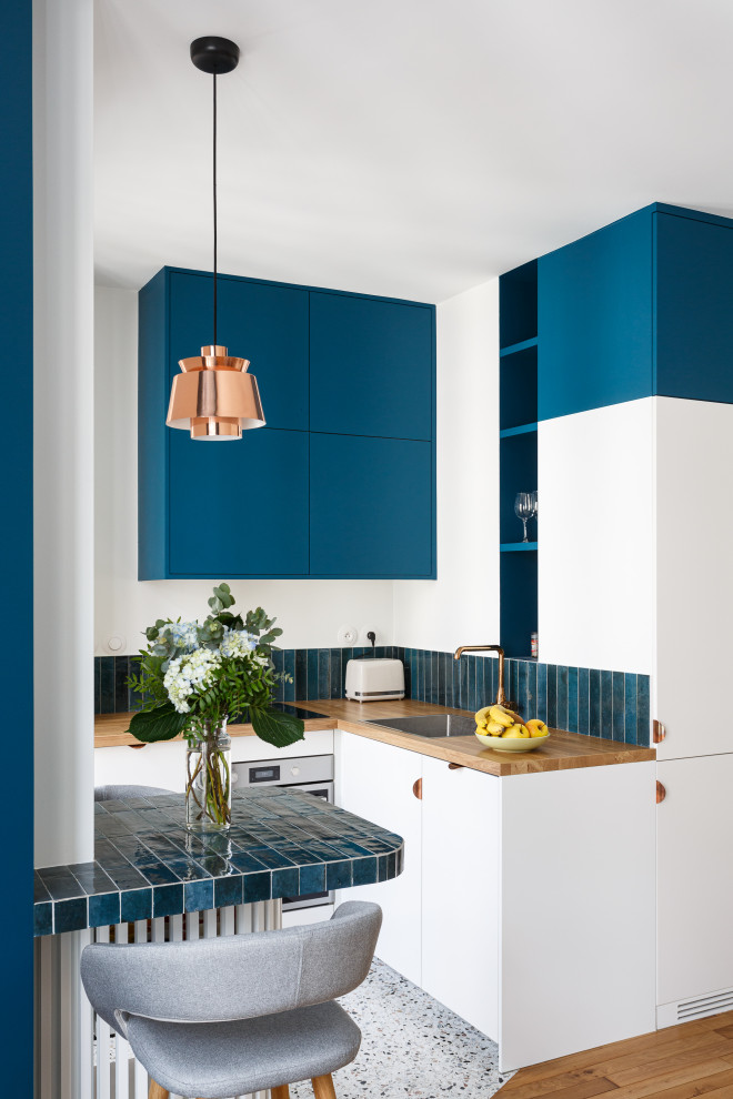 Foto på ett litet funkis brun kök, med en enkel diskho, släta luckor, blå skåp, träbänkskiva, blått stänkskydd, stänkskydd i keramik, integrerade vitvaror, terrazzogolv och flerfärgat golv