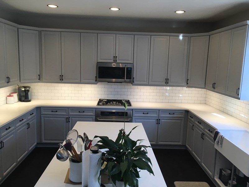 Example of a large transitional u-shaped dark wood floor and brown floor enclosed kitchen design in Atlanta with a farmhouse sink, raised-panel cabinets, white backsplash, subway tile backsplash, stainless steel appliances, an island, white cabinets and quartzite countertops