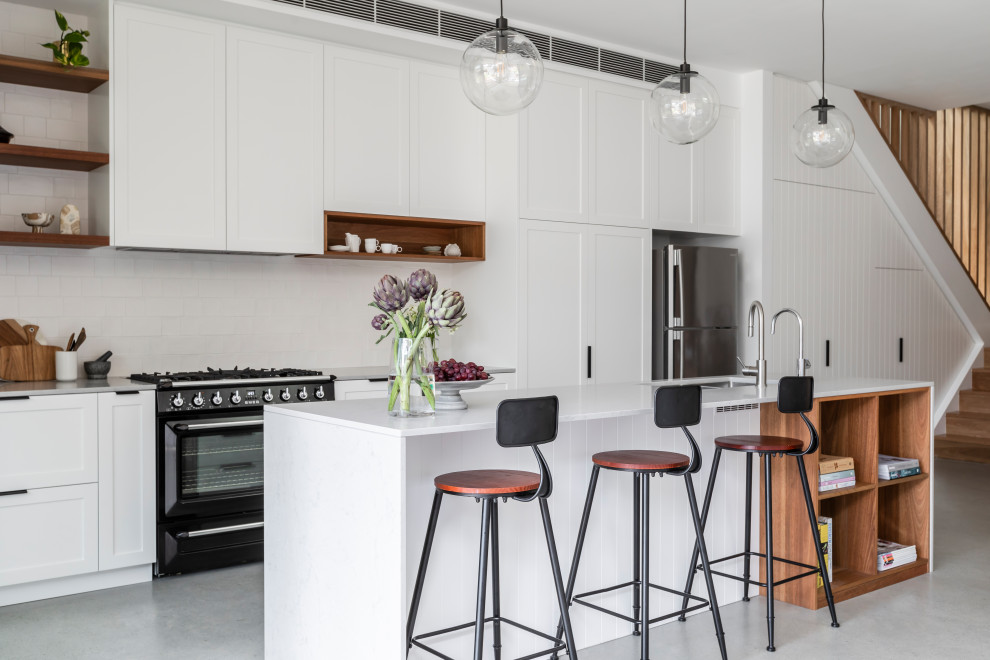 Inspiration for a mid-sized transitional single-wall open plan kitchen in Sydney with an undermount sink, shaker cabinets, white cabinets, quartz benchtops, white splashback, ceramic splashback, black appliances, concrete floors, with island, grey floor and grey benchtop.