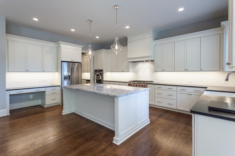 Inspiration for a transitional u-shaped medium tone wood floor and brown floor open concept kitchen remodel in DC Metro with a farmhouse sink, recessed-panel cabinets, white cabinets, white backsplash, subway tile backsplash, stainless steel appliances, an island and black countertops