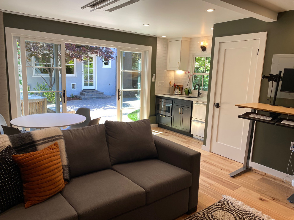 Cette image montre une petite salle de séjour traditionnelle ouverte avec un mur vert, parquet clair, un téléviseur fixé au mur et un sol beige.