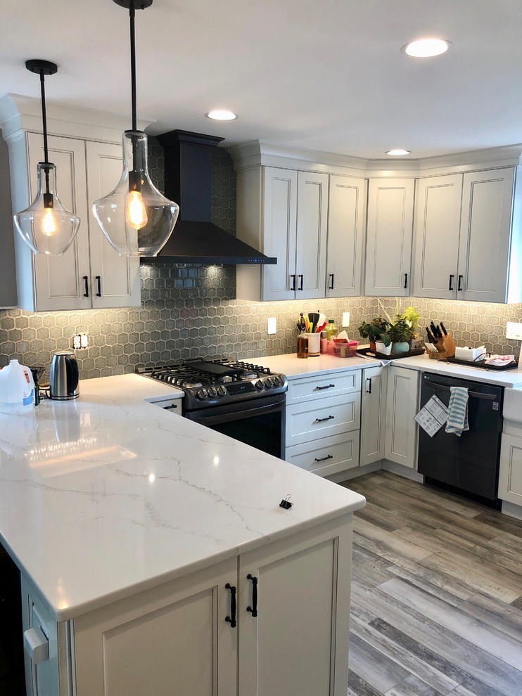 Photo of a large transitional u-shaped eat-in kitchen in Philadelphia with a farmhouse sink, recessed-panel cabinets, beige cabinets, quartz benchtops, grey splashback, porcelain splashback, black appliances, vinyl floors, a peninsula, multi-coloured floor and white benchtop.