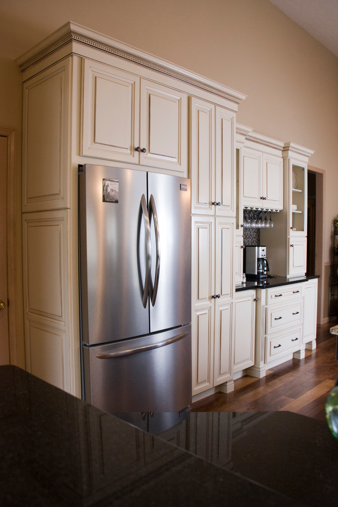 Example of a large transitional l-shaped medium tone wood floor eat-in kitchen design with an undermount sink, raised-panel cabinets, distressed cabinets, granite countertops, black backsplash, stainless steel appliances and an island