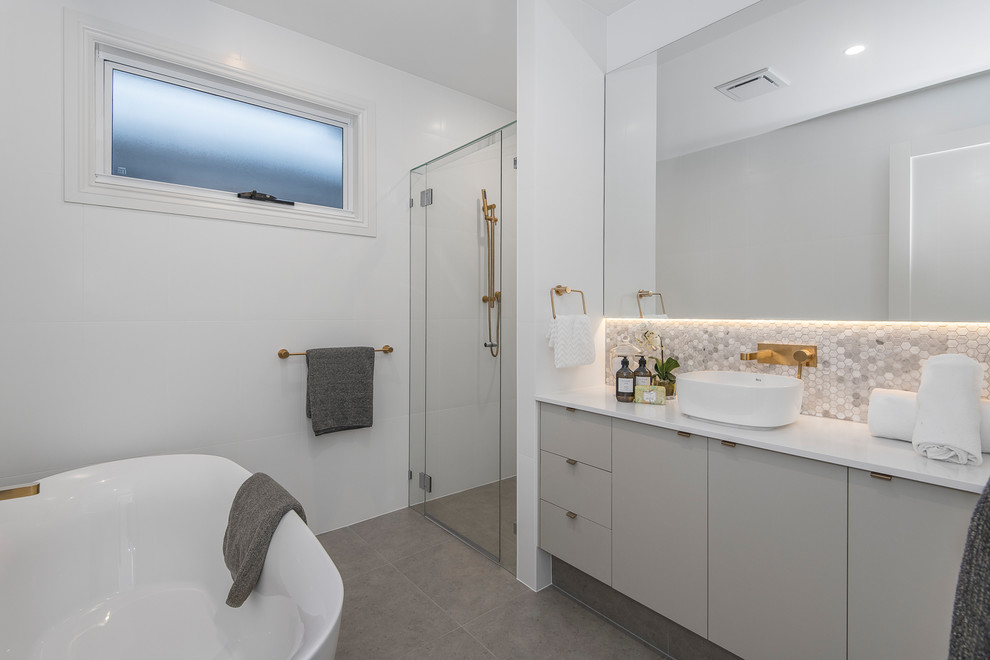 Inspiration for a small traditional kids bathroom in Brisbane with recessed-panel cabinets, grey cabinets, a freestanding tub, an alcove shower, gray tile, marble, white walls, porcelain floors, a console sink, engineered quartz benchtops, grey floor, a hinged shower door and grey benchtops.