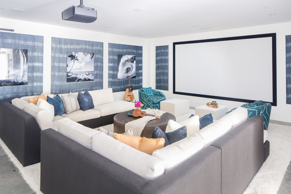 Large beach style open concept home theatre in Orange County with white walls, concrete floors, a projector screen and grey floor.
