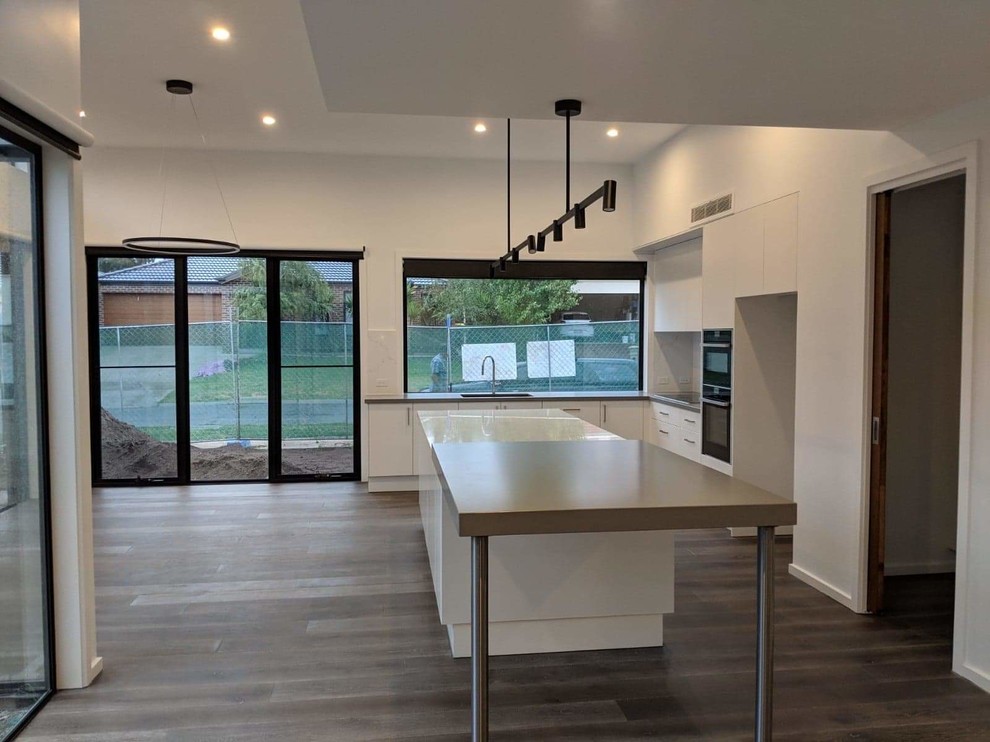 Photo of a mid-sized modern l-shaped eat-in kitchen in Melbourne with an undermount sink, flat-panel cabinets, white cabinets, quartz benchtops, black appliances, laminate floors, with island and grey benchtop.