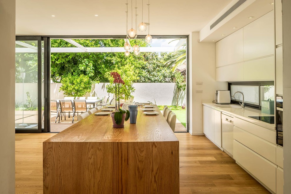 Inspiration for a small modern galley open plan kitchen in Tel Aviv with a drop-in sink, flat-panel cabinets, white cabinets, wood benchtops, stainless steel appliances, light hardwood floors and with island.