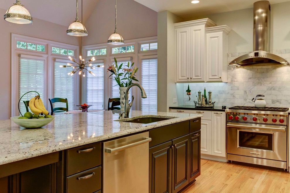 Eat-in kitchen - mid-sized transitional galley light wood floor eat-in kitchen idea in Raleigh with a double-bowl sink, raised-panel cabinets, white cabinets, granite countertops, white backsplash, stone tile backsplash, stainless steel appliances and an island