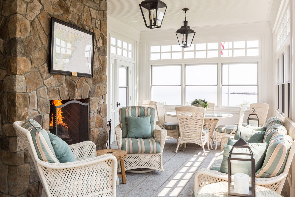 Beach style sunroom in Portland Maine with a standard fireplace, a stone fireplace surround, a standard ceiling and grey floor.