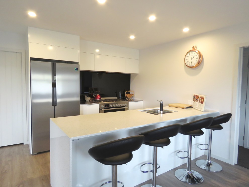 Design ideas for a mid-sized modern galley eat-in kitchen in Napier-Hastings with a double-bowl sink, white cabinets, quartz benchtops, black splashback, glass sheet splashback, stainless steel appliances, vinyl floors and with island.