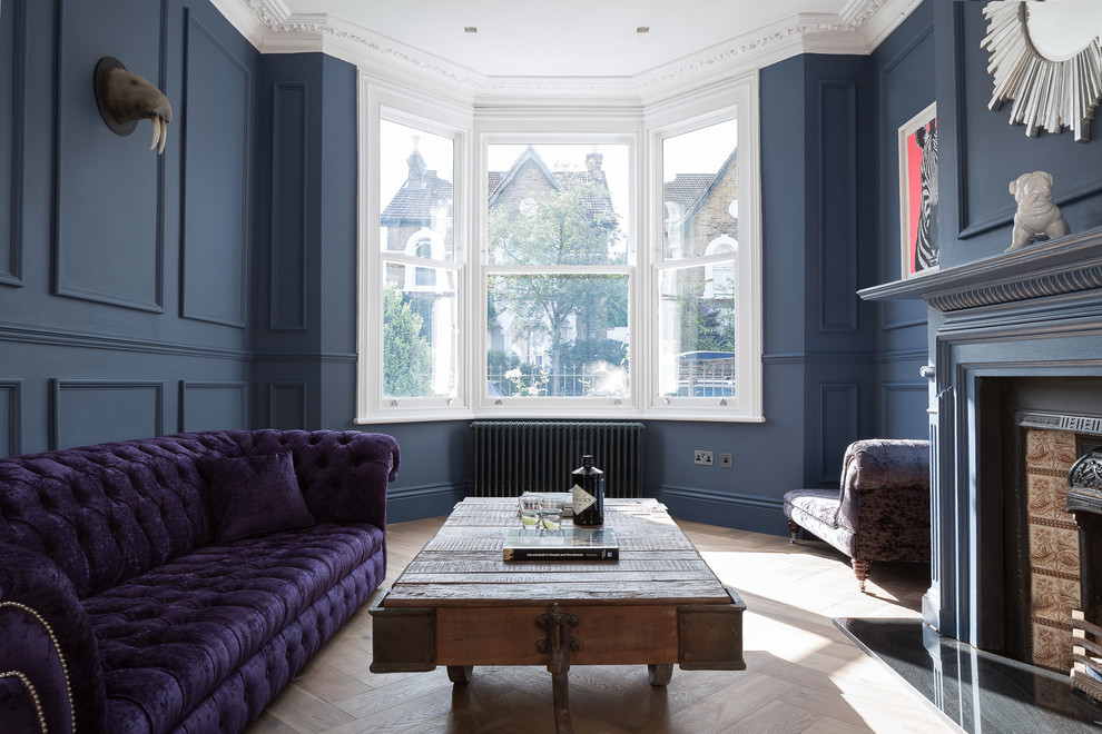 This is an example of an eclectic formal enclosed living room in London with blue walls, medium hardwood floors, a standard fireplace, a tile fireplace surround and no tv.