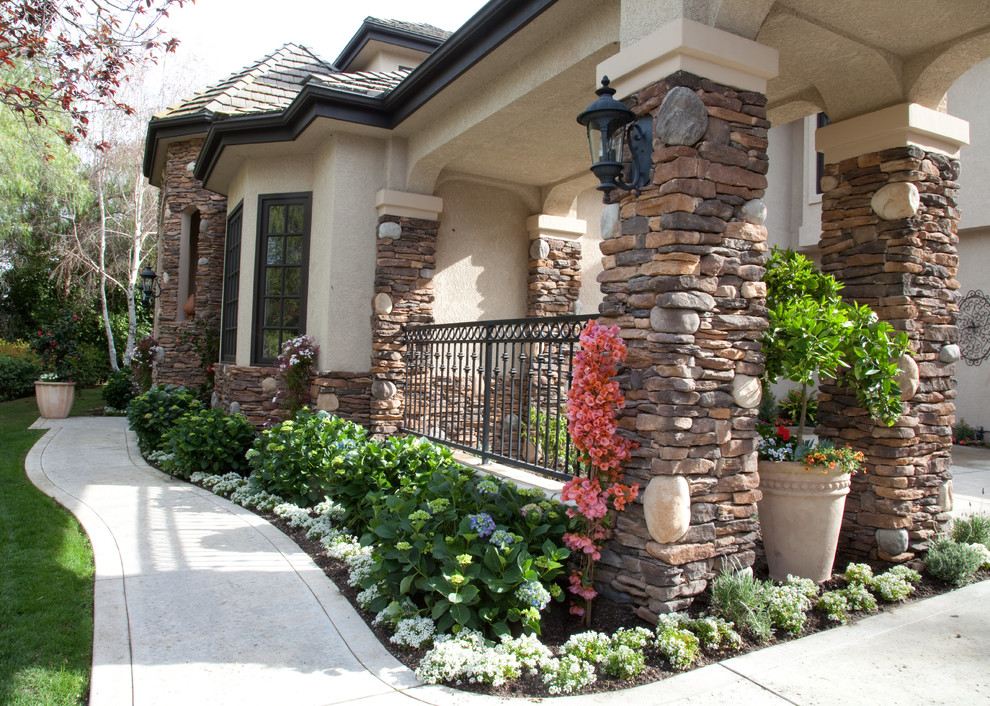 This is an example of a mid-sized mediterranean front yard partial sun formal garden for spring in Orange County with a garden path, concrete pavers and a metal fence.