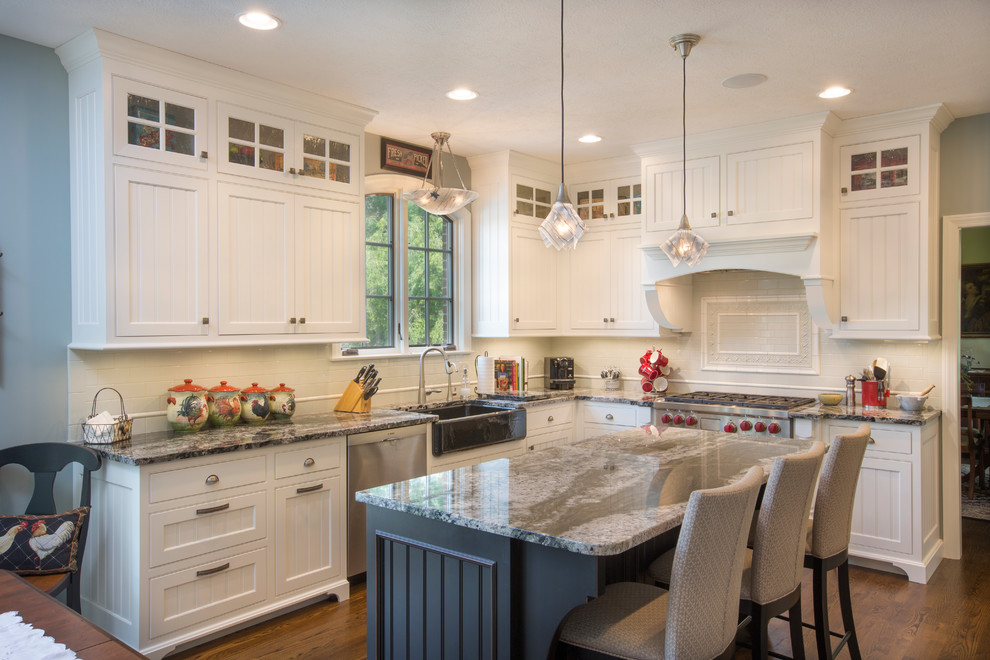 Photo of a traditional l-shaped kitchen in Columbus with a farmhouse sink, recessed-panel cabinets, white cabinets, white splashback, stainless steel appliances, dark hardwood floors and with island.