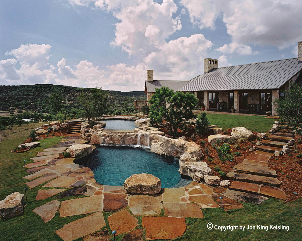 Photo of an expansive country backyard custom-shaped natural pool in Austin with a water feature and natural stone pavers.
