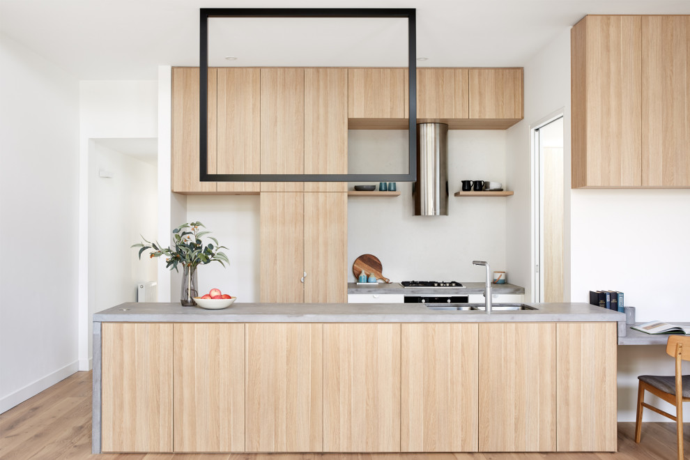 Photo of a small contemporary u-shaped open plan kitchen in Melbourne with a drop-in sink, recessed-panel cabinets, light wood cabinets, concrete benchtops, white splashback, stone slab splashback, stainless steel appliances, light hardwood floors, no island and grey benchtop.