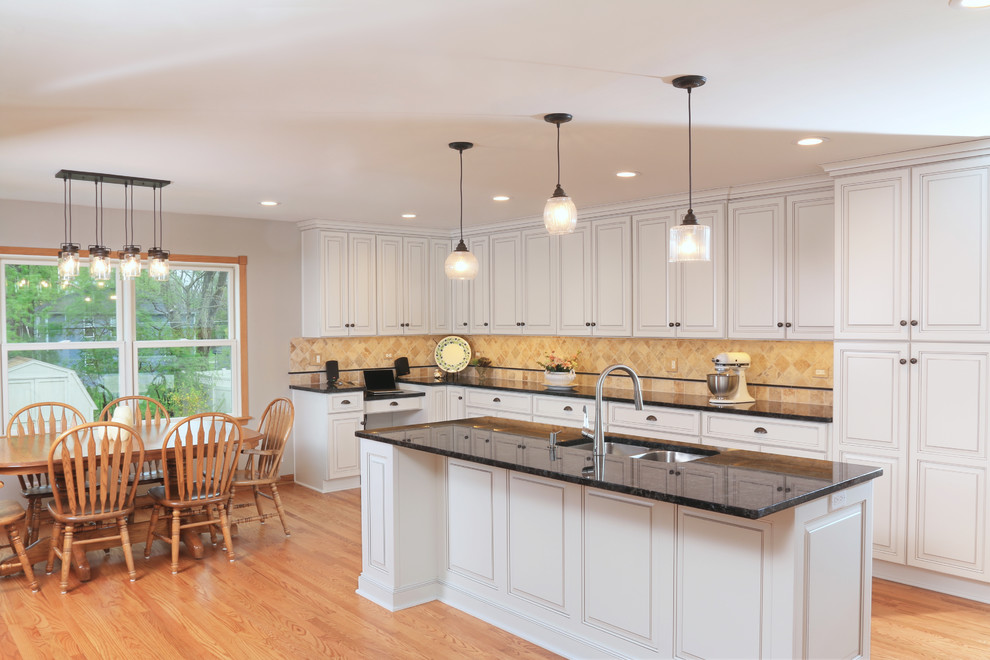 Photo of a large contemporary l-shaped eat-in kitchen in Chicago with a double-bowl sink, raised-panel cabinets, white cabinets, beige splashback, ceramic splashback, white appliances, light hardwood floors, with island and beige floor.