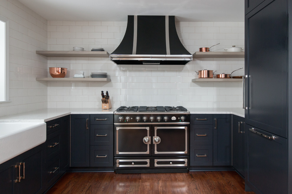 Inredning av ett modernt litet kök, med en rustik diskho, skåp i shakerstil, svarta skåp, bänkskiva i kvarts, vitt stänkskydd, stänkskydd i tunnelbanekakel, svarta vitvaror och mellanmörkt trägolv