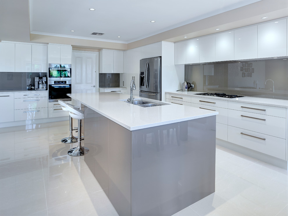Inspiration for an expansive contemporary open plan kitchen with an undermount sink, white cabinets, grey splashback, glass sheet splashback, stainless steel appliances and with island.