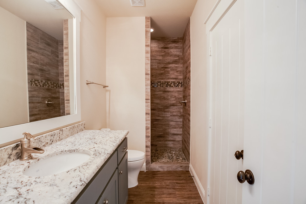 Design ideas for a mid-sized traditional kids bathroom in Dallas with shaker cabinets, blue cabinets, a drop-in tub, an alcove shower, brown tile, ceramic tile, beige walls, medium hardwood floors, an undermount sink, granite benchtops, brown floor and an open shower.